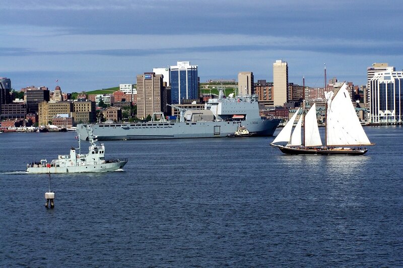 Sailboat and naval ships in harbor