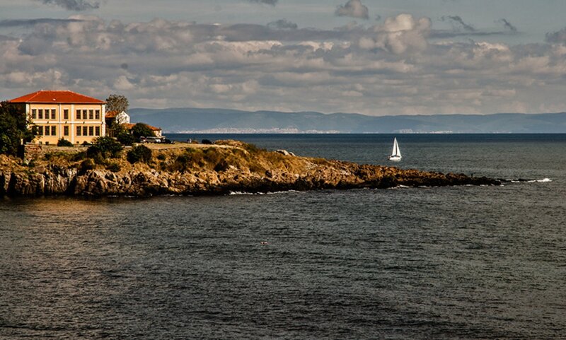 Sailboat Near Rocky Coast — Blue, Serene, Afternoon, Photograph, Building