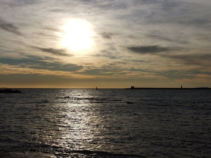 Sailboat on Ocean — Blue, Serene, Sunset, Photograph, Sun, Clouds, Lighthouse