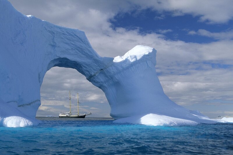 Sailboat under Ice Arch — Blue, Serene, Afternoon, Photograph, Iceberg, Ocean