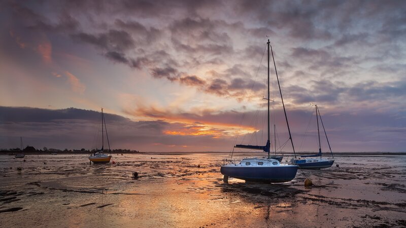 Sailboats on a muddy shore at sunset