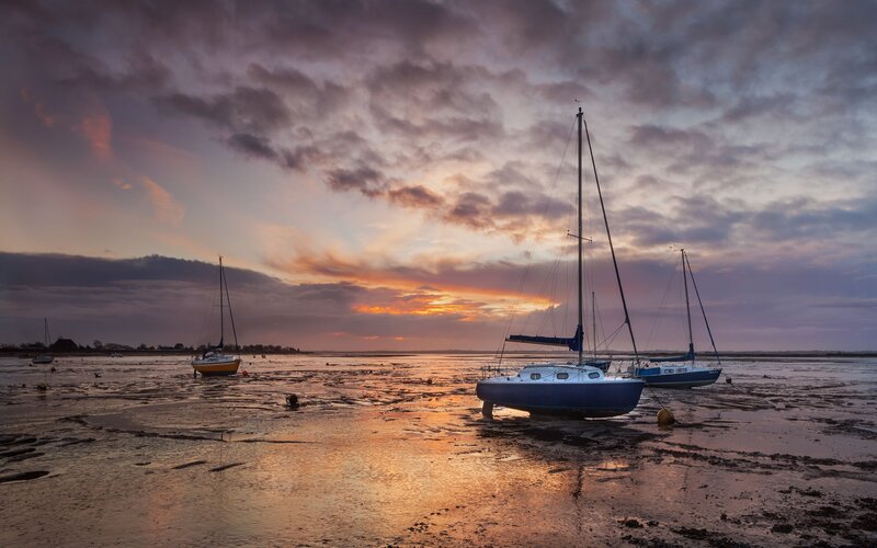 Sailboats on a muddy shore at sunset