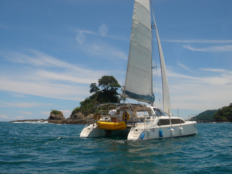 Sailing catamaran near rocky island