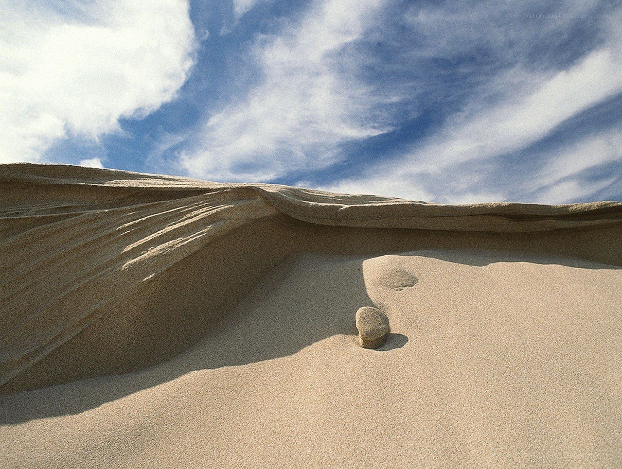 Sand dune with stone under blue sky