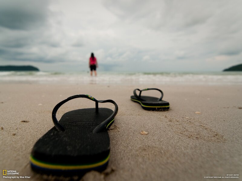 Sandal on beach with person in distance