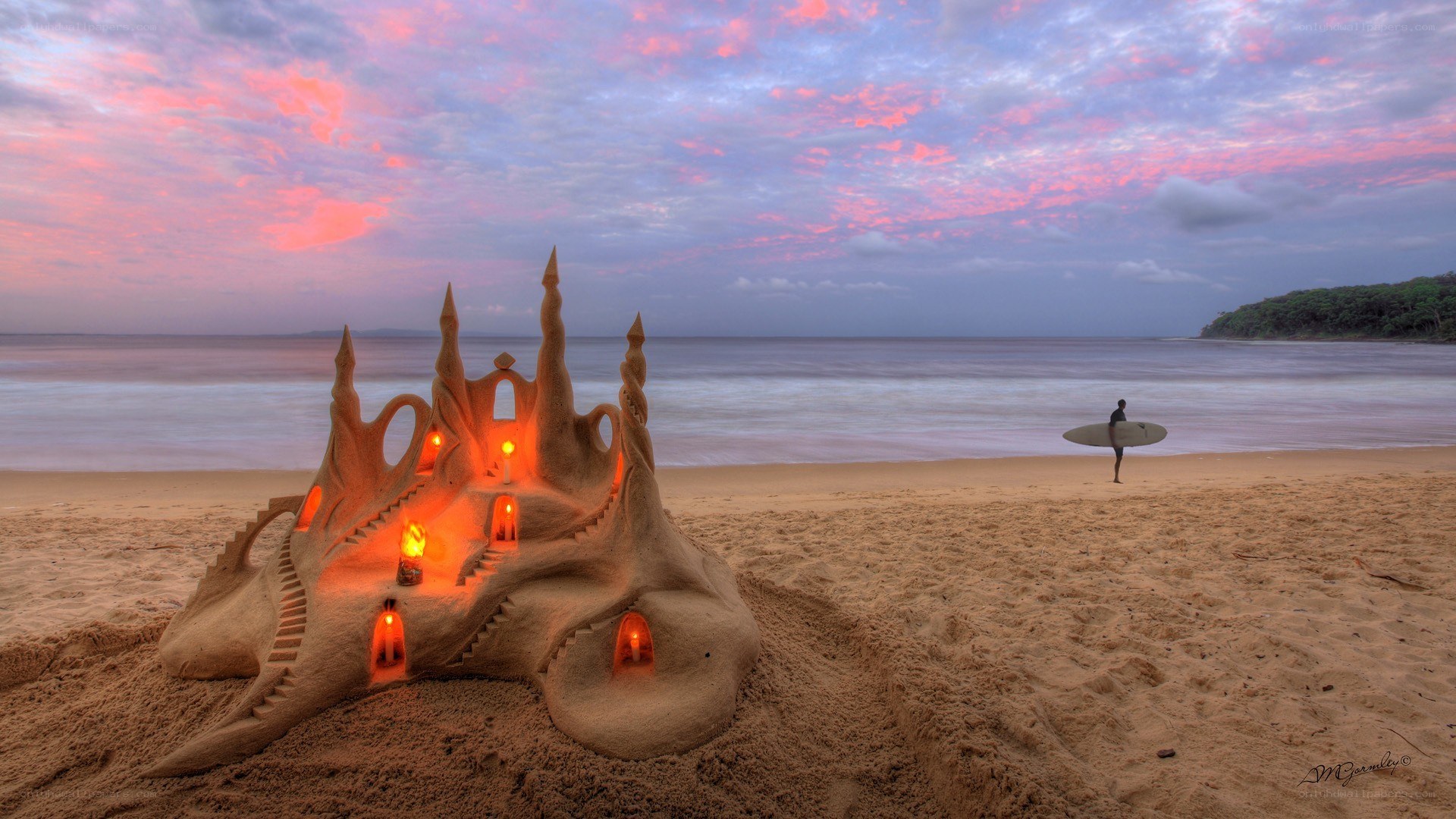 Sandcastle at sunset with surfer