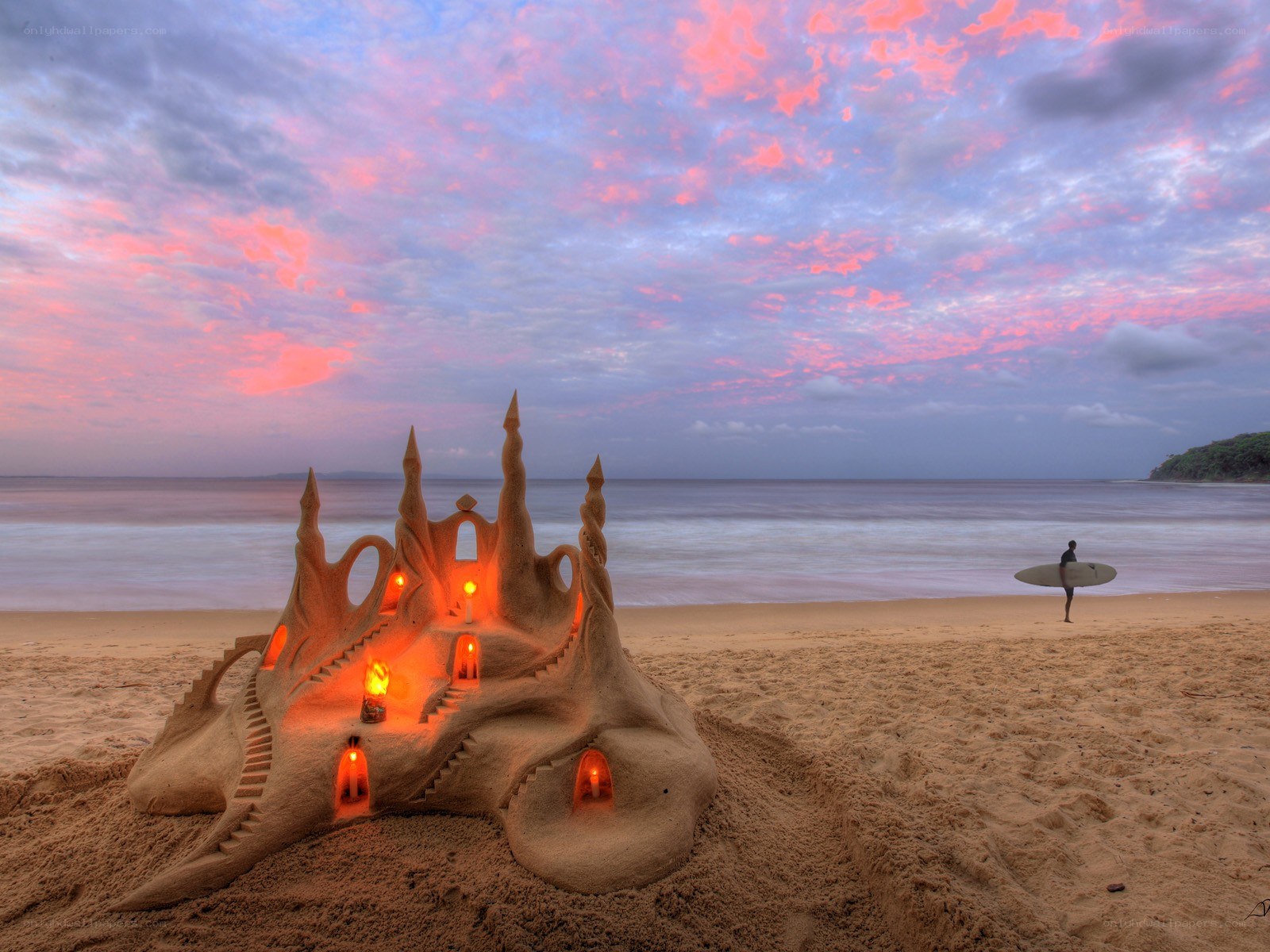Sandcastle at sunset with surfer