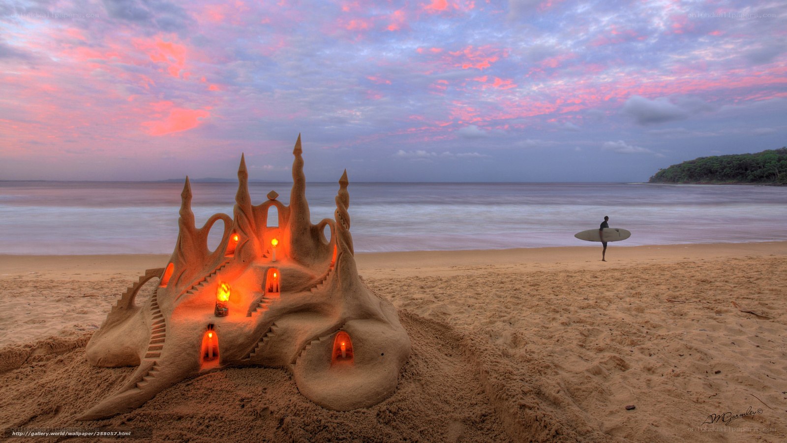 Sandcastle at sunset with surfer