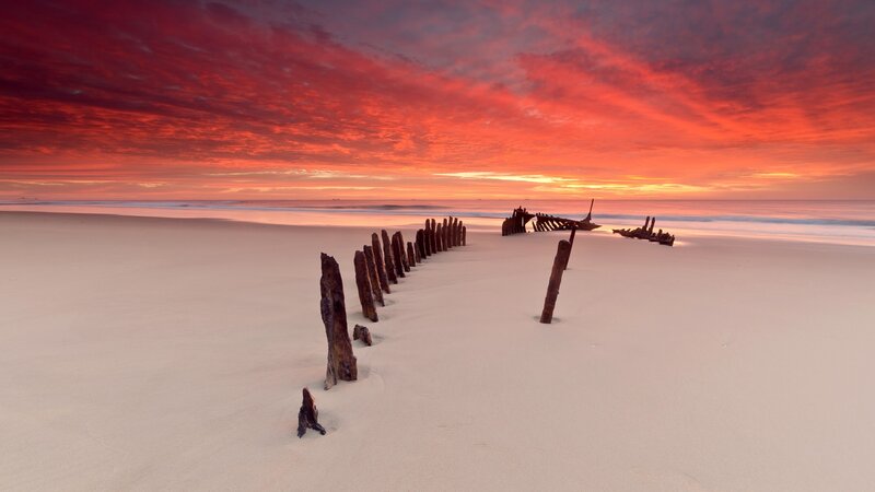 Shipwreck on Beach — Red, Dramatic, Sunset, Photograph, Wooden Posts