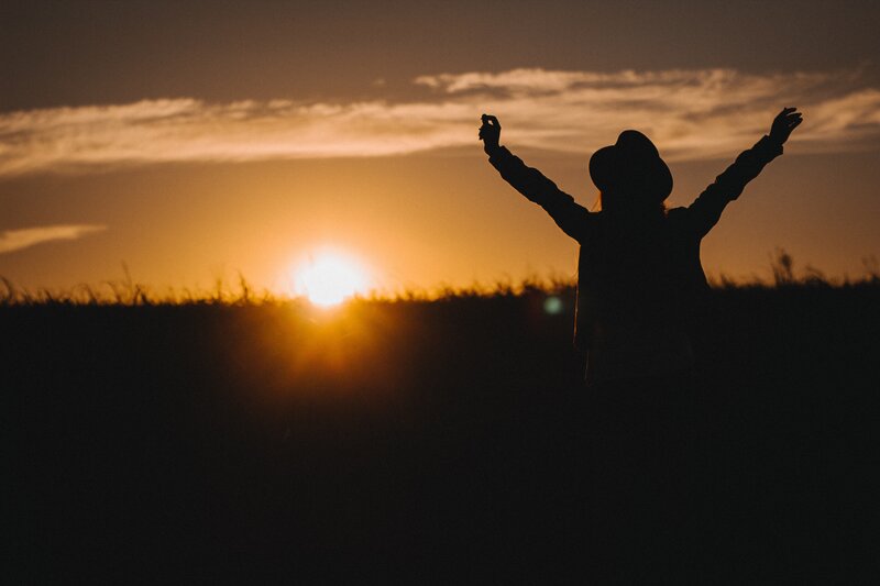 silhouette at sunset with arms raised