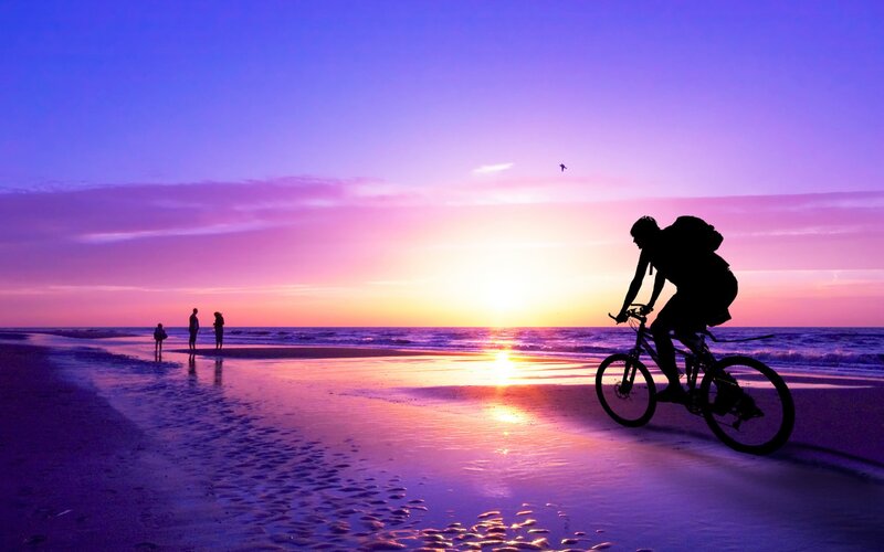 Silhouette cyclist on beach at sunset