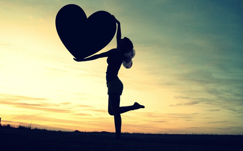 silhouette holding heart at sunset