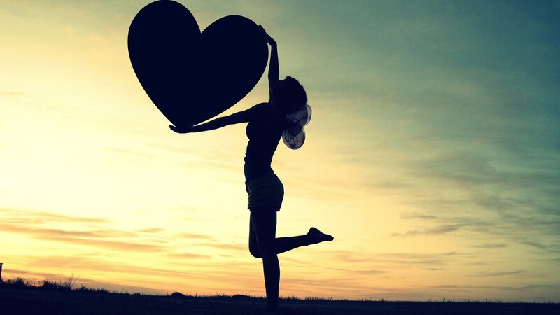 silhouette holding heart at sunset