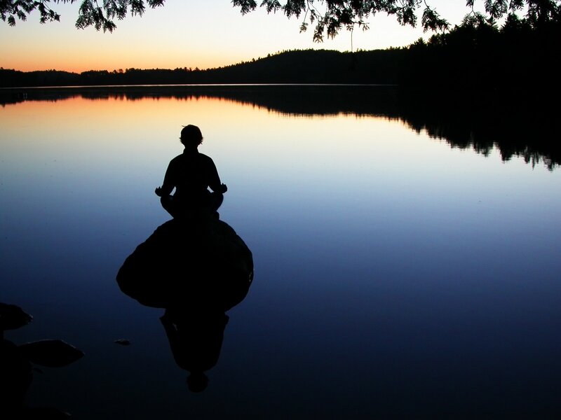 Silhouette meditating by a lake
