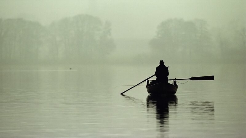 Silhouette of a fisherman on a misty lake