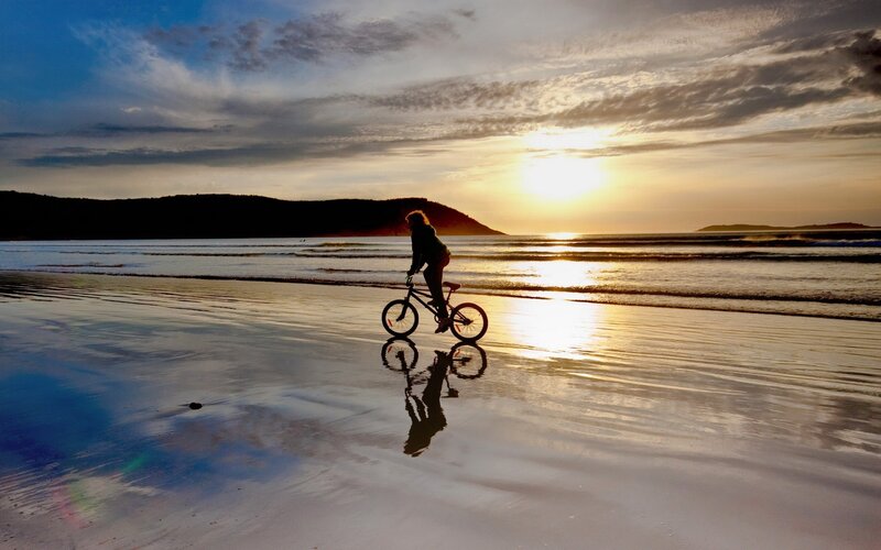 Silhouette of cyclist on beach at sunset