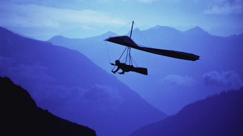 Silhouette of hang glider over mountains