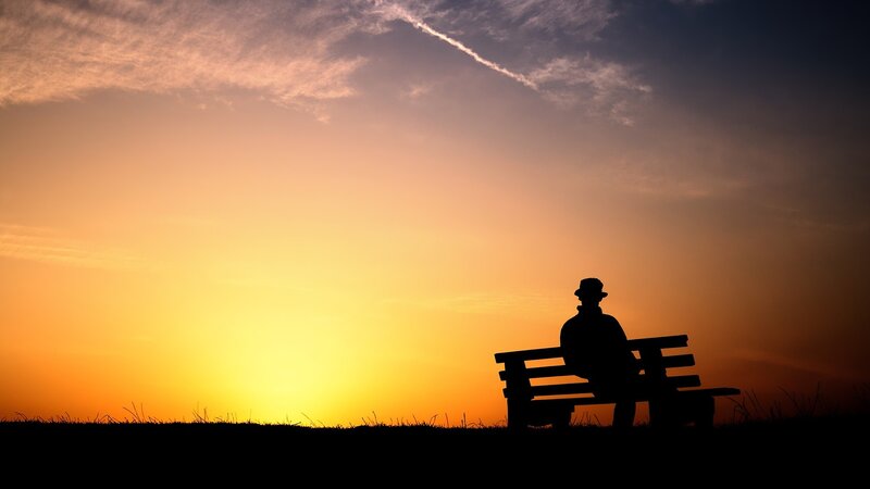 Silhouette of man on bench at sunset