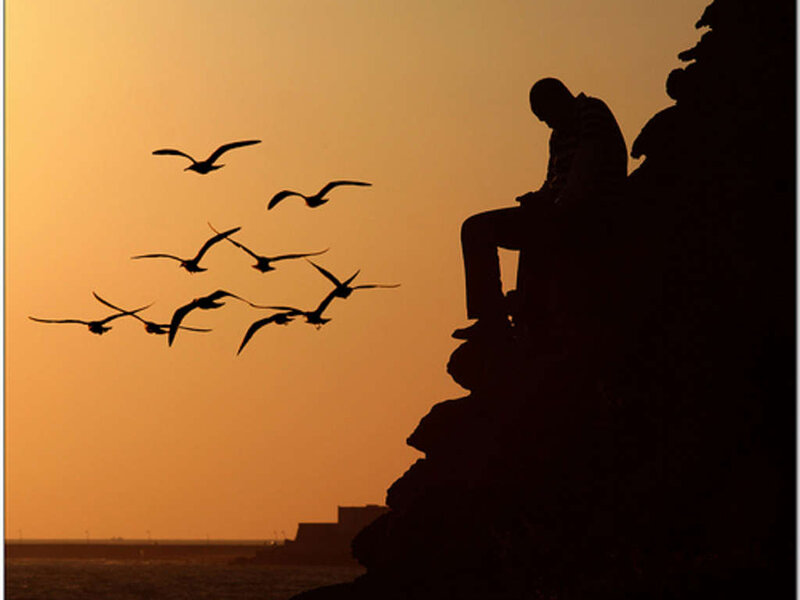 Silhouette of man on cliff at sunset