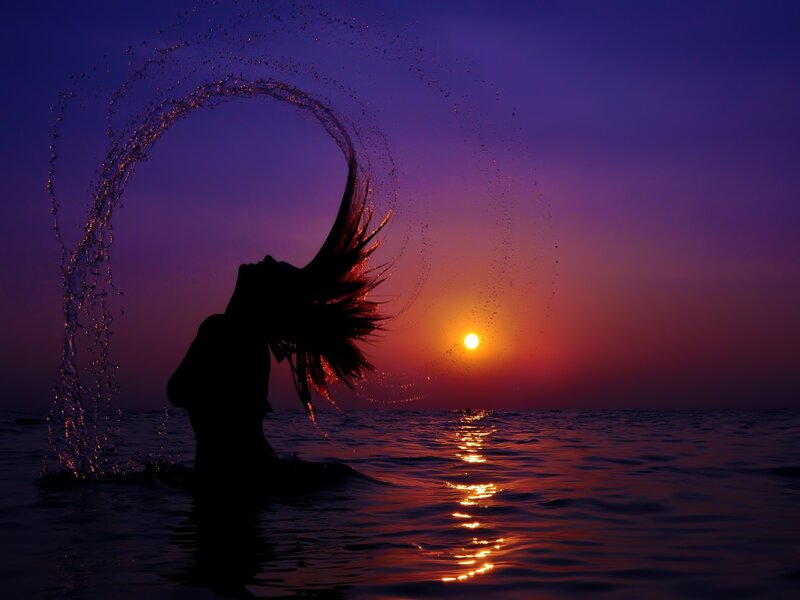 Silhouette of woman in ocean at sunset