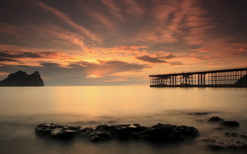 Silhouetted Pier at Sunset — Orange, Serene, Photograph, Rocky Island