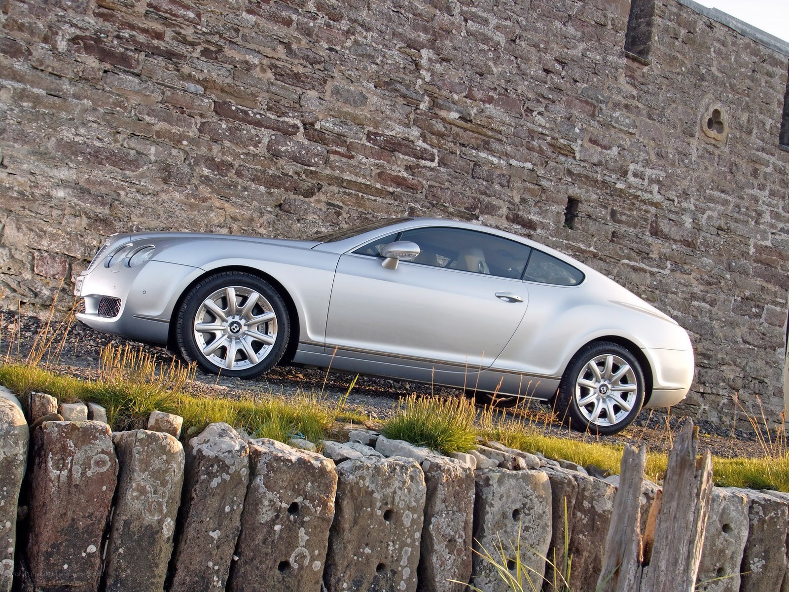 Silver Bentley parked by stone wall