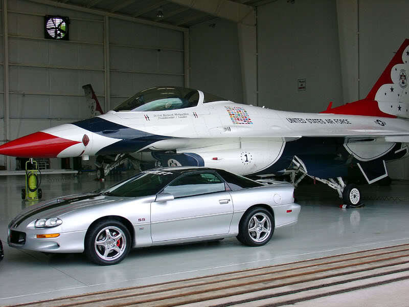 Silver car and fighter jet in hangar