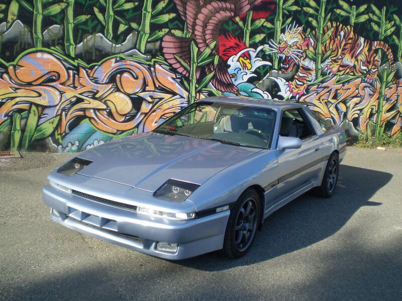 Silver car in front of graffiti wall