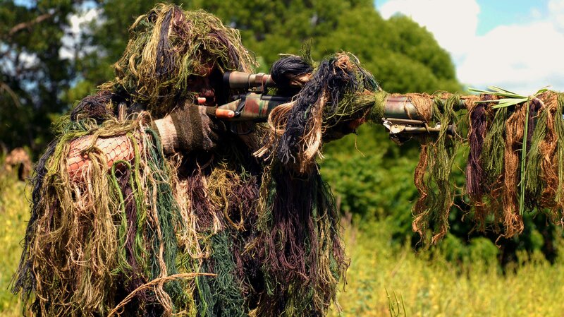 sniper in ghillie suit aiming rifle
