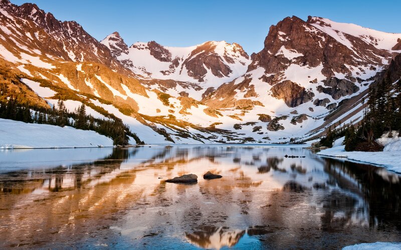 Snow-capped mountains reflect in a calm lake
