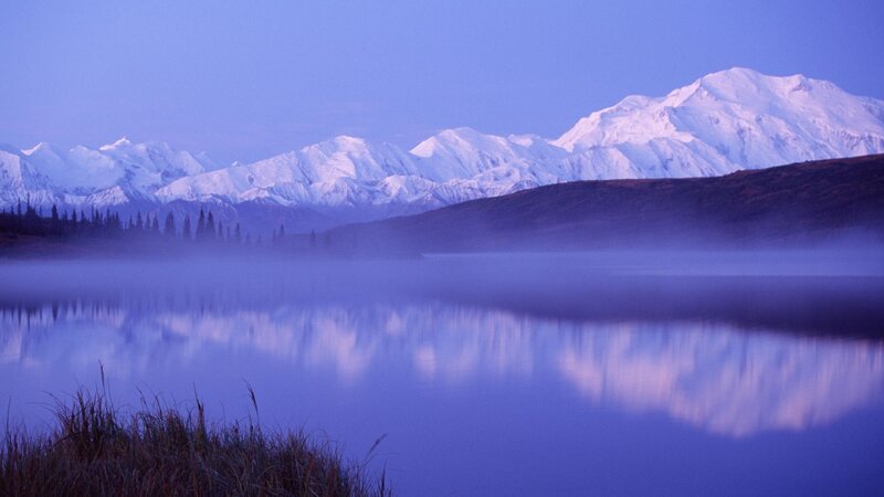 Snow-capped mountains reflect in a misty lake
