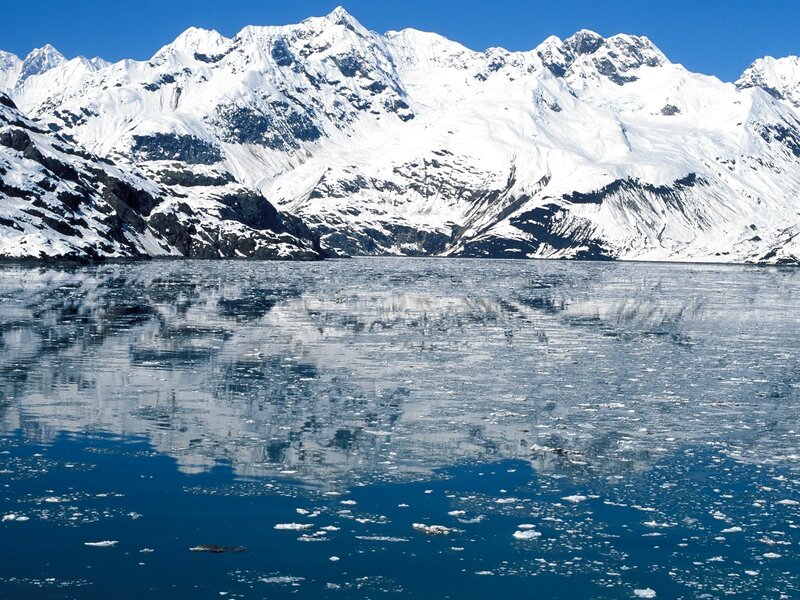 Snow-capped mountains reflect in icy water
