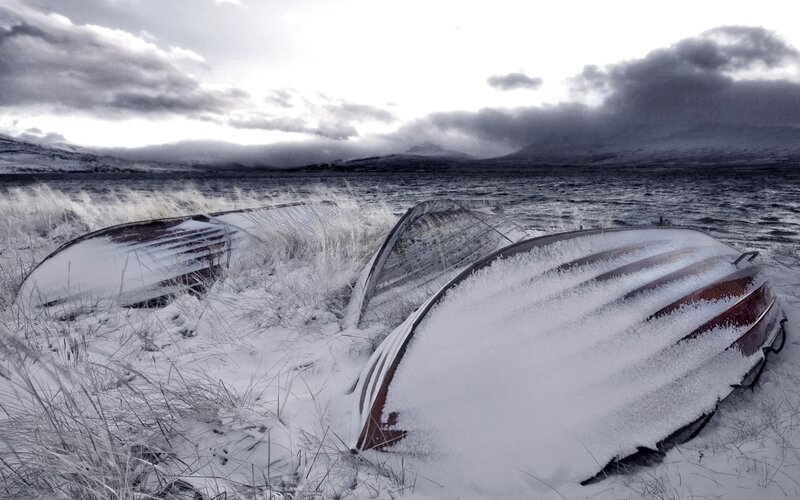 Snow-covered boats on a lake shore