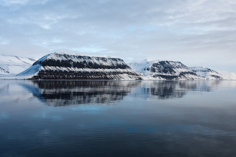 Snow-covered mountains reflect in calm water