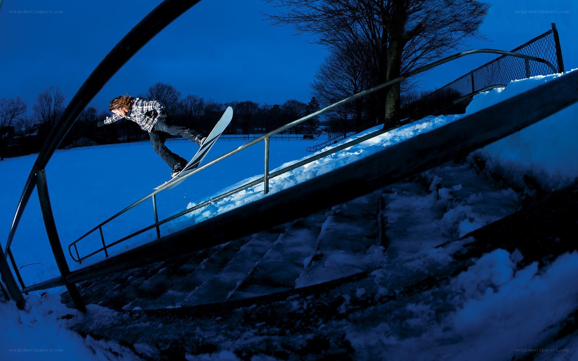 Snowboarder grinding rail at dusk