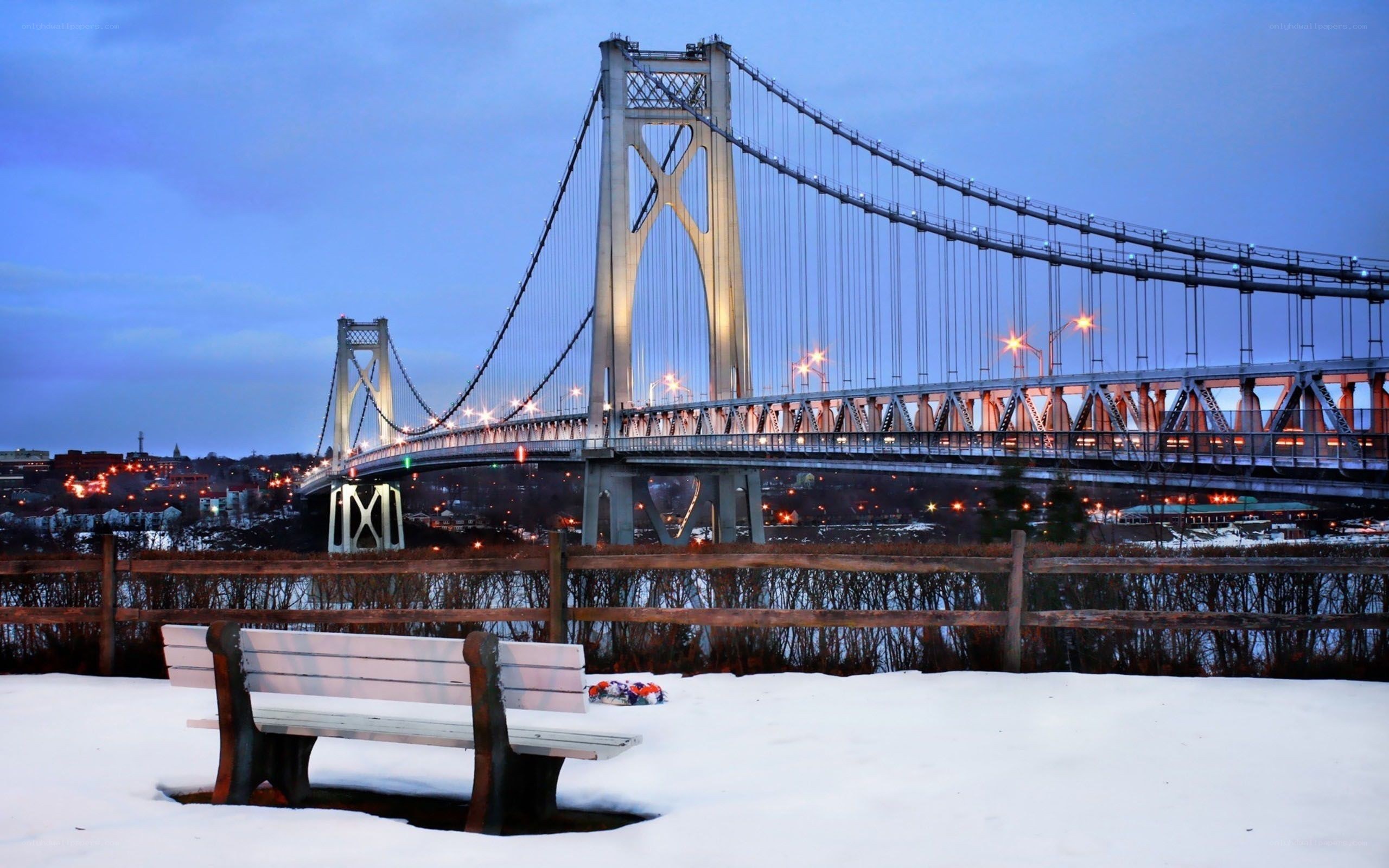 Snowy bench by a lit bridge