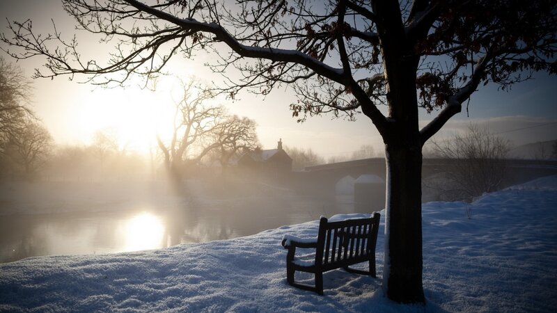 Snowy bench by river at sunrise