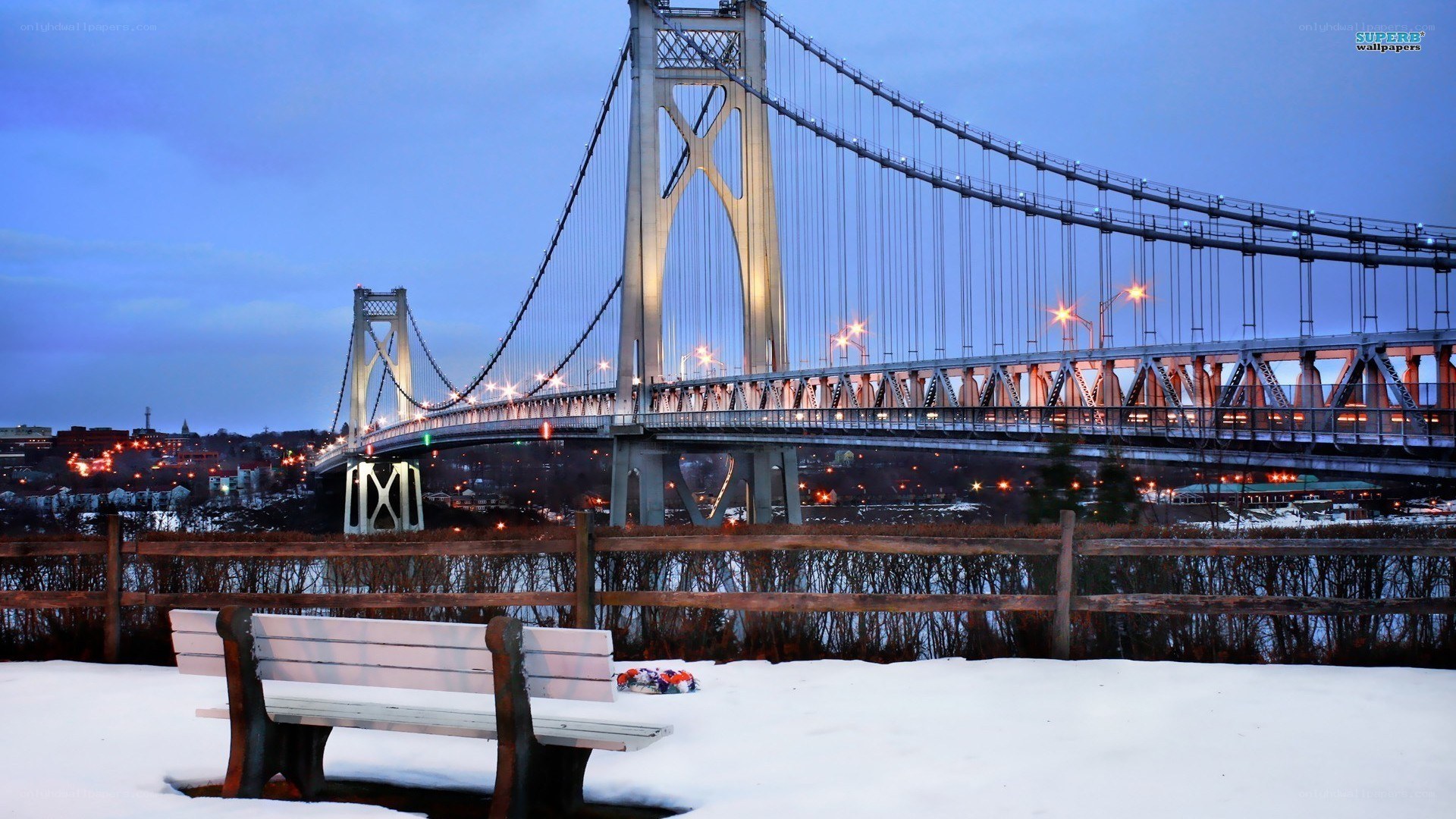 Snowy bench by suspension bridge
