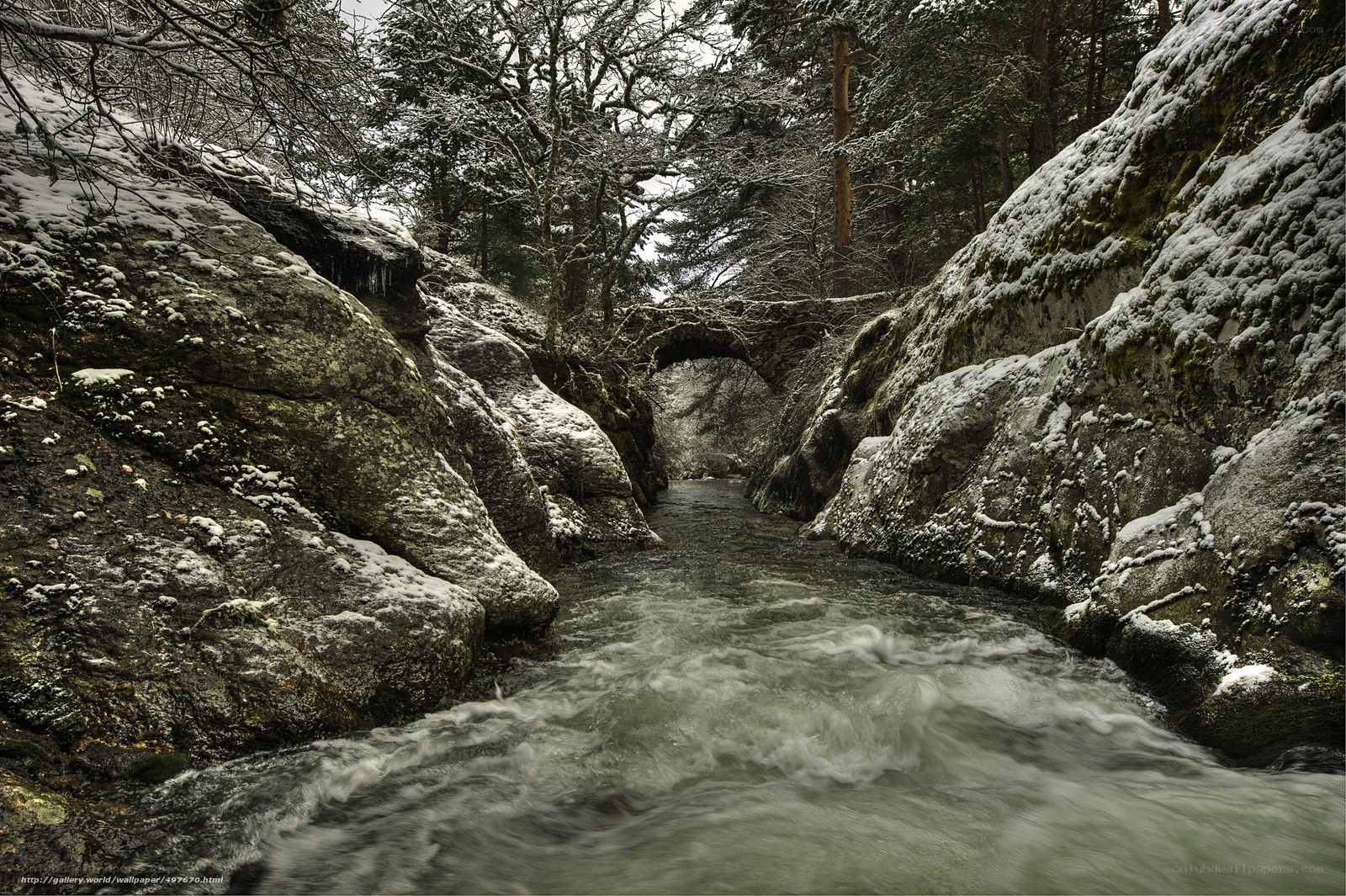 Snowy river gorge with stone bridge