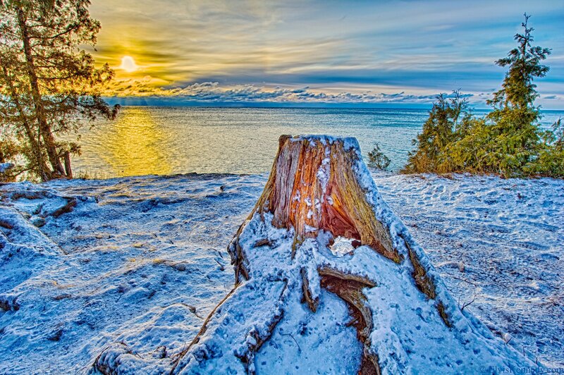 Snowy stump at sunset by the lake