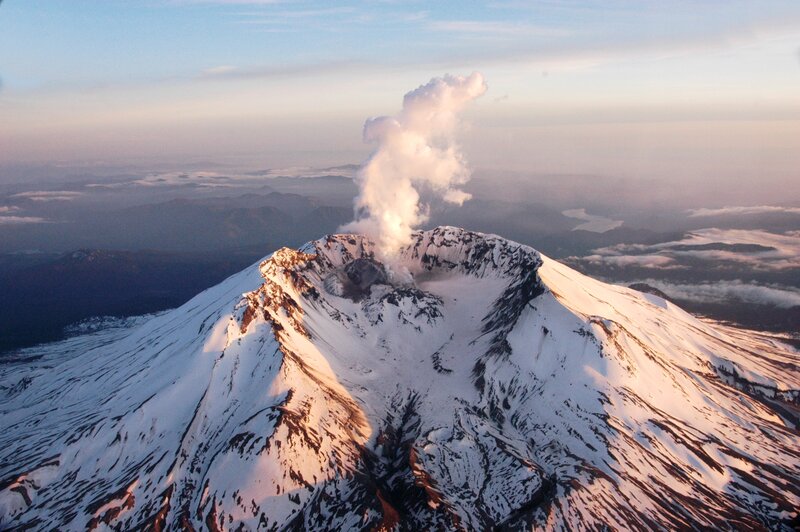 Snowy volcano erupting at sunrise