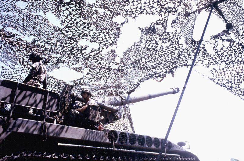 Soldiers on tank under camouflage net