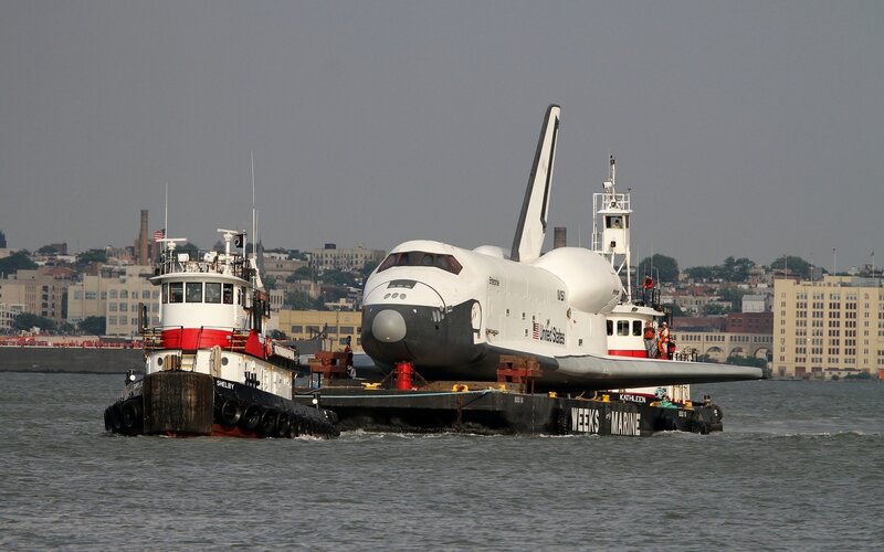 Space shuttle being transported by tugboats