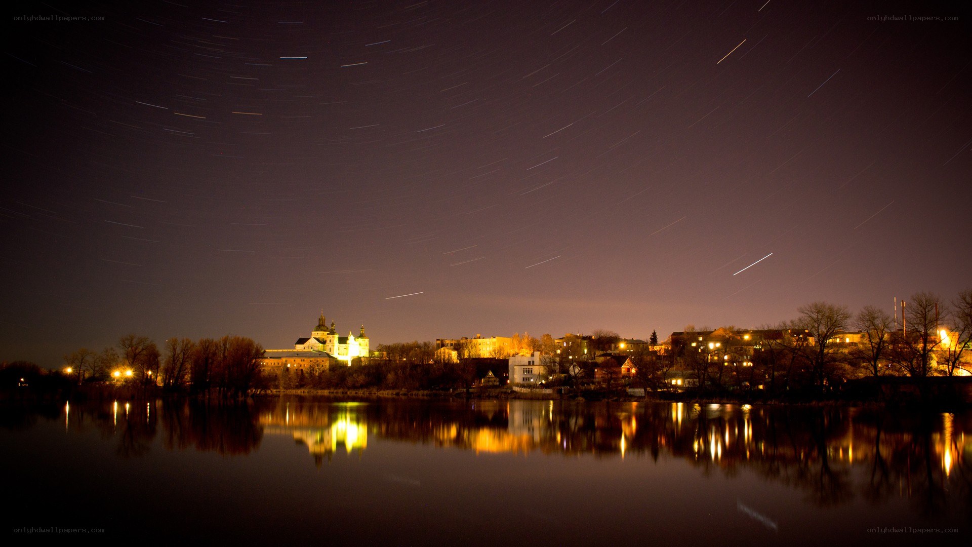 Star trails over a riverside town