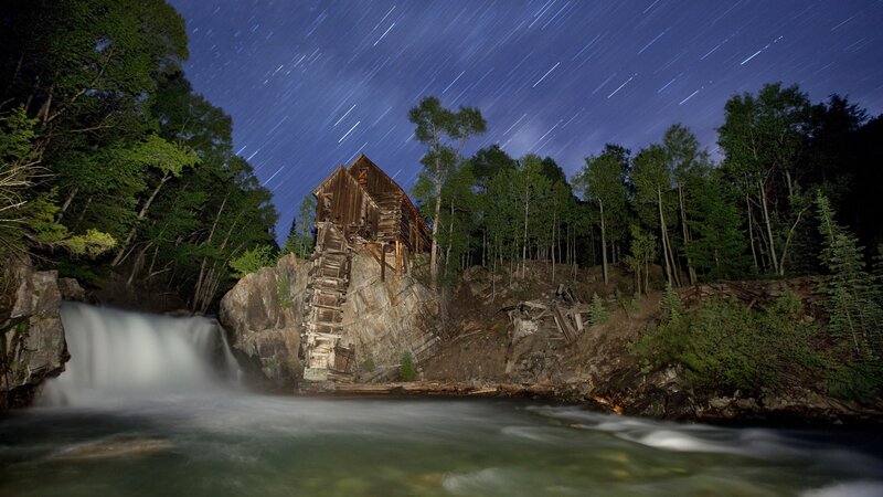 Star trails over a waterfall mill