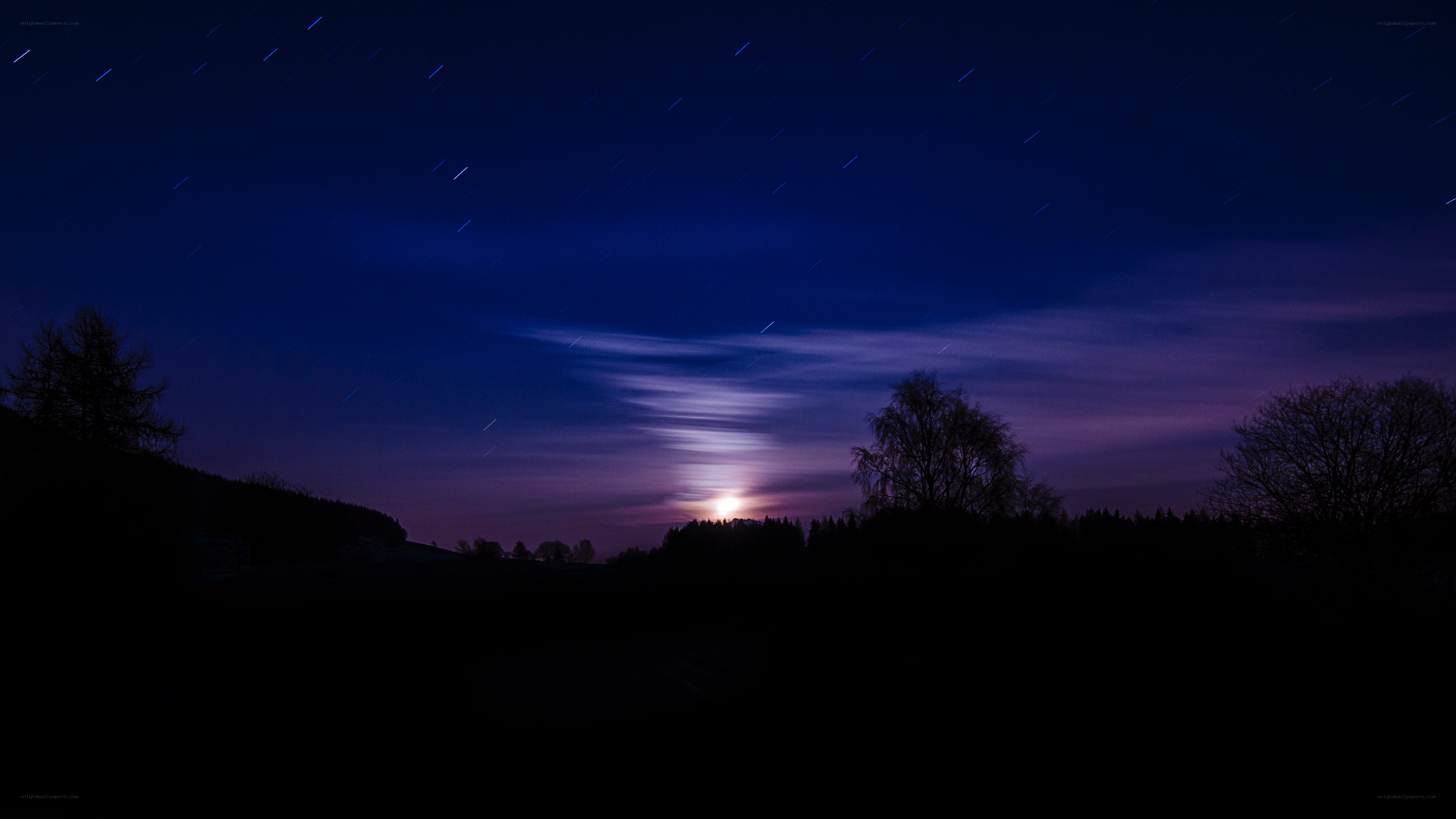 Star trails over moonlit landscape