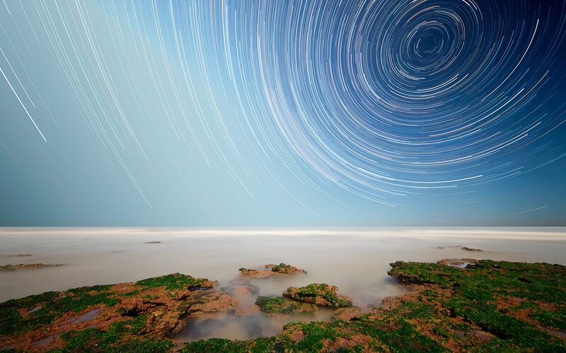 Star trails over rocky shore