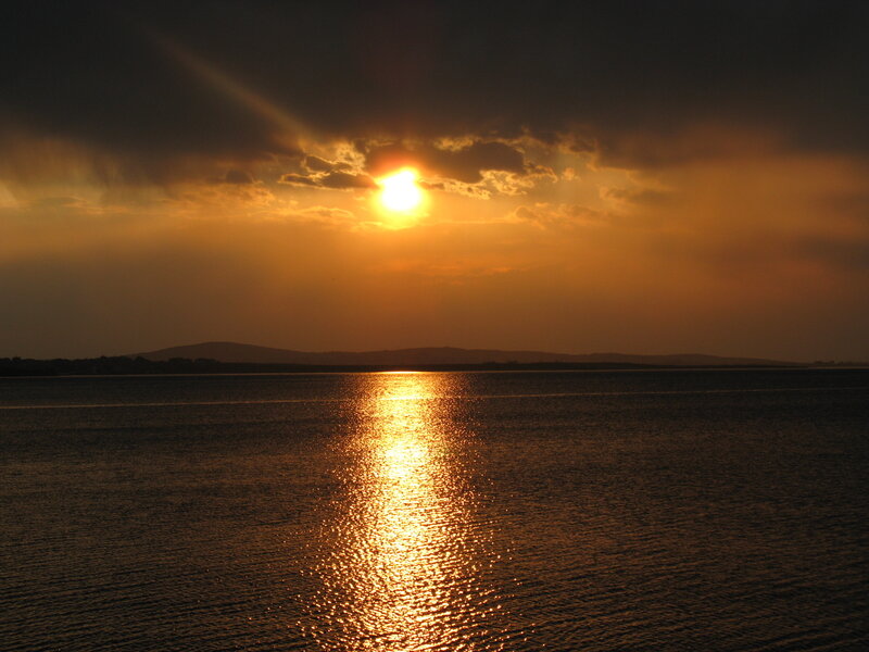 Sun Setting over Water — Orange, Dramatic, Sunset, Photograph, Clouds, Mountains, Black