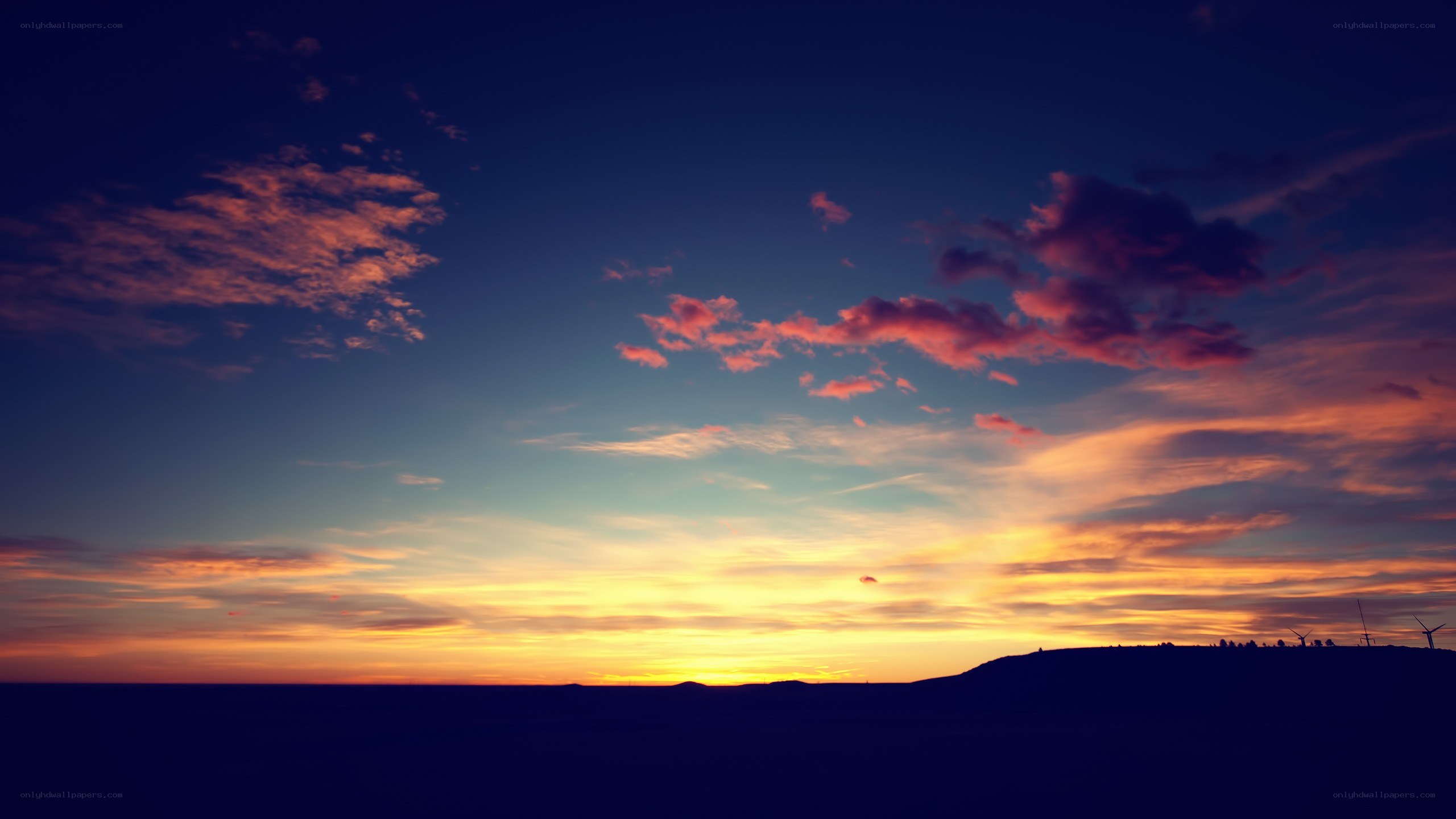 sunset over a hill with wind turbines