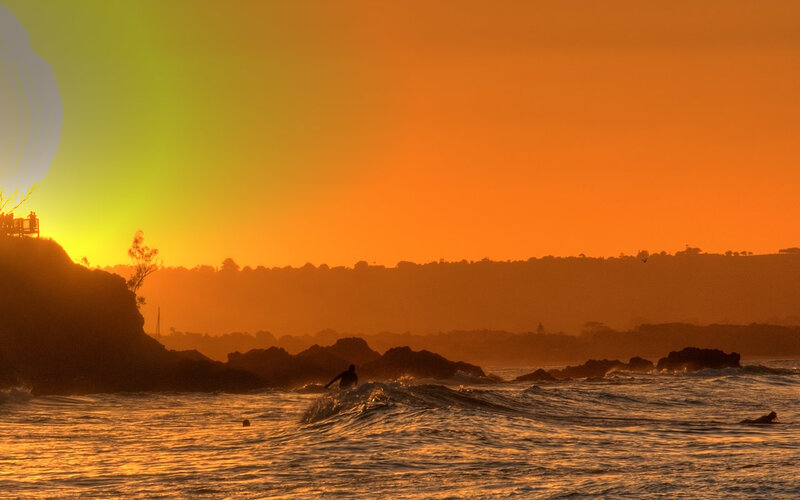 Surfer at sunset on rocky coast